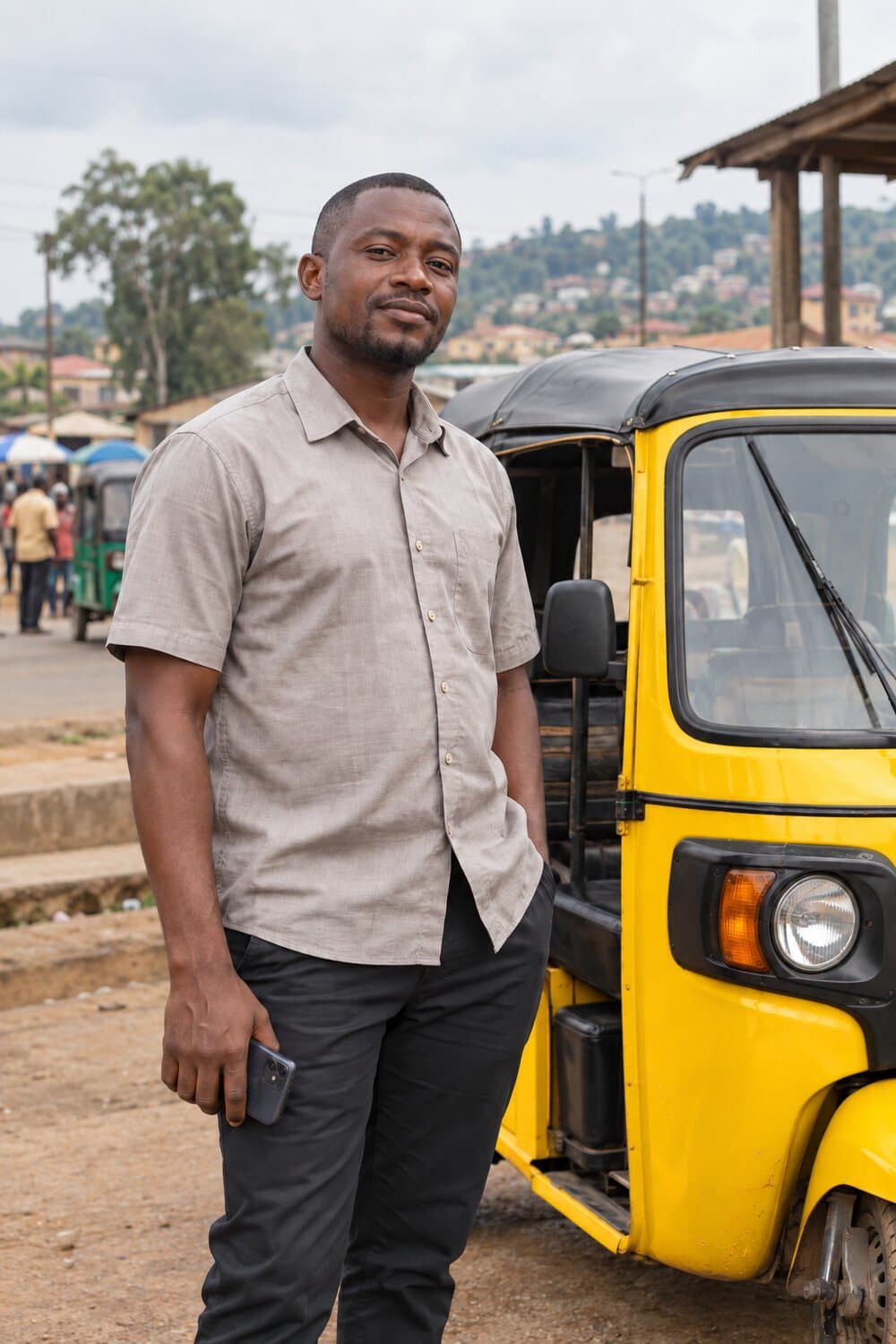 A keke rider standing beside a yellow tricycle at a neighborhood rank